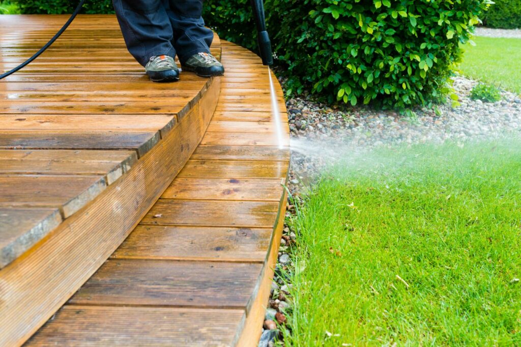 Person pressure-washing a wooden deck.