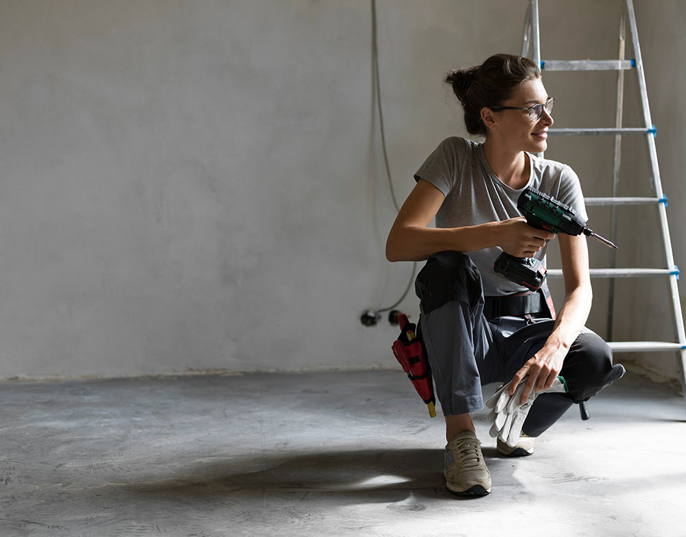 Worker holding an impact driver kneeling in front of a ladder.