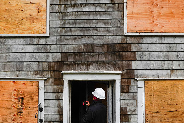 Person looking at a damaged building with boarded up windows.