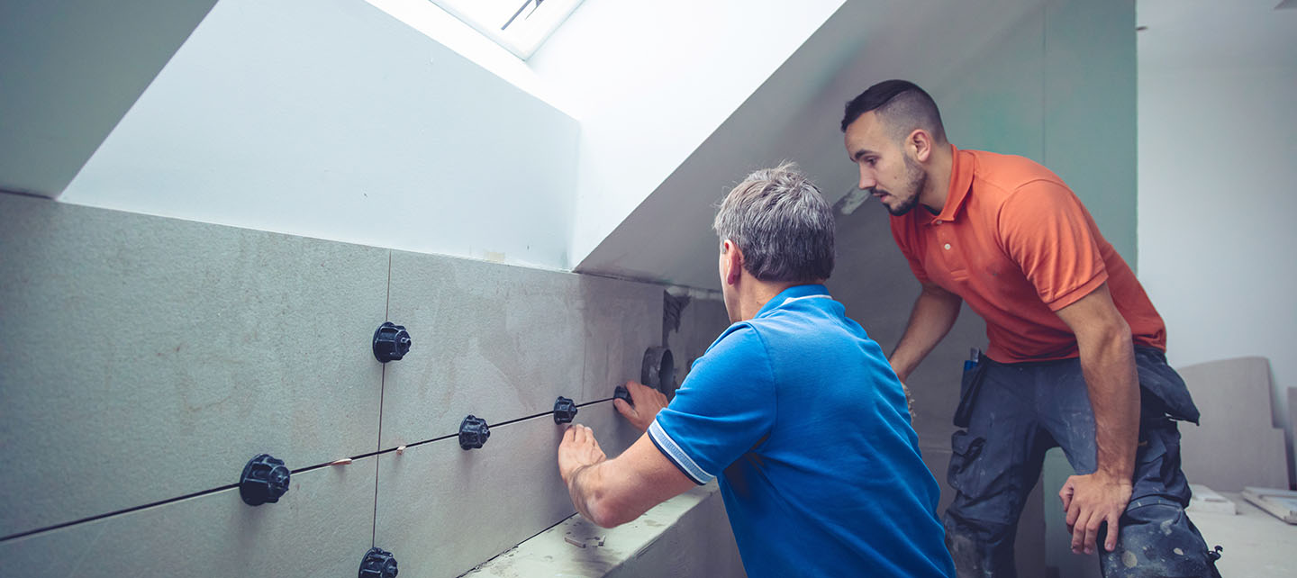 Man teaching a younger man how to install large wall tiles.